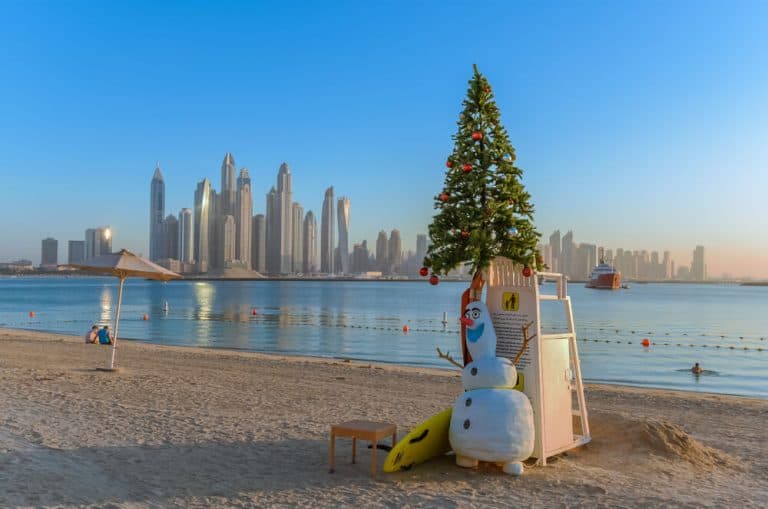 Christmas tree and snowman on a sandy beach overlooking the Dubai Marina skyscrapers
